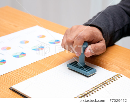 Close up Asian businessman holding rubber stamp and stamping with approved stamp 77029452