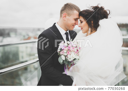 Lovely happy wedding couple, bride with long white dress posing in beautiful city Lovely happy wedding couple, bride with long white dress posing in beautiful city 77030268