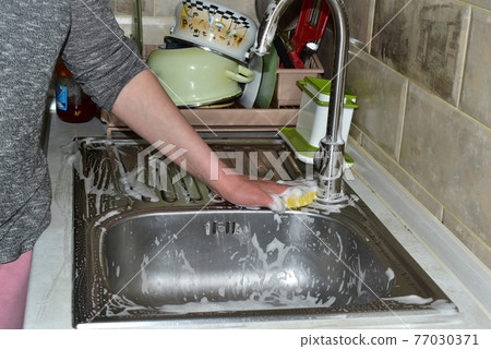 A woman washes the metal surface of the sink with a washcloth. 77030371