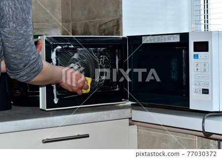 A woman washes the microwave with a washcloth. 77030372