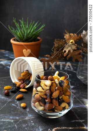 Mix of delicious assorted nuts and dried fruit in white cups on a table, sunny morning. Healthy gourmet vegetarian natural snack. Mix of delicious assorted nuts and dried fruit in white cups on a table, sunny morning. Healthy gourmet vegetarian natural snack. 77030422