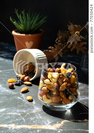 Mix of delicious assorted nuts and dried fruit in white cups on a table, sunny morning. Healthy gourmet vegetarian natural snack. 77030424