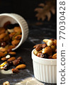 Mix of delicious assorted nuts and dried fruit in white cups on a table, sunny morning. Healthy gourmet vegetarian natural snack. 77030428