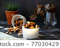 Mix of delicious assorted nuts and dried fruit in white cups on a table, sunny morning. Healthy gourmet vegetarian natural snack. 77030429