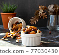 Mix of delicious assorted nuts and dried fruit in white cups on a table, sunny morning. Healthy gourmet vegetarian natural snack. 77030430