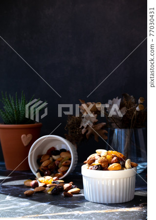 Mix of delicious assorted nuts and dried fruit in white cups on a table, sunny morning. Healthy gourmet vegetarian natural snack. 77030431
