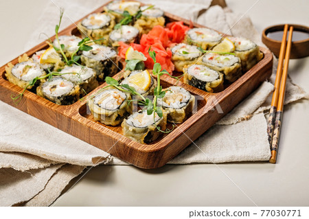 Hot rolls with eel, Japanese omelette, cream cheese, fried onions and unagi sauce, decorated with fresh herbs. Japanese food on a bamboo platter, bamboo sticks, sauce on a light background. Copy space 77030771