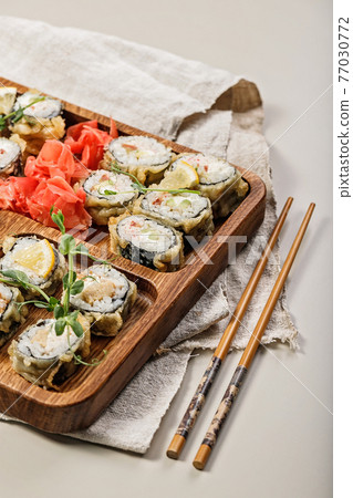 Hot rolls with eel, Japanese omelette, cream cheese, fried onions and unagi sauce, decorated with fresh herbs. Japanese food on a bamboo platter, bamboo sticks on a light background. Vertical shot 77030772
