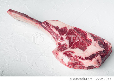Raw uncooked black angus beef tomahawk steak on bone, on white stone background, with copy space for text 77032057
