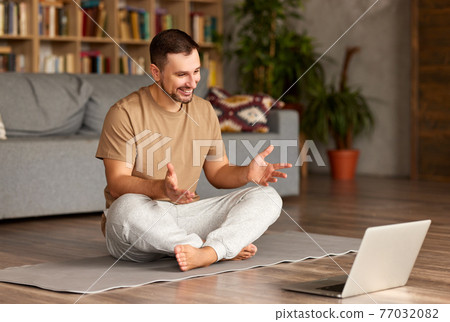 Young man in casual wear sitting in front of laptop in lotus pose and practicing yoga online Young man in casual wear sitting in front of laptop in lotus pose and practicing yoga online 77032082