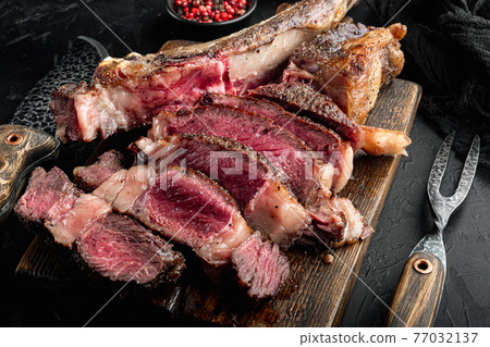 Slices of Medium rare grilled marbled meat beef steak, tomahawk cut, on wooden serving board, on black stone background Slices of Medium rare grilled marbled meat beef steak, tomahawk cut, on wooden serving board, on black stone background 77032137