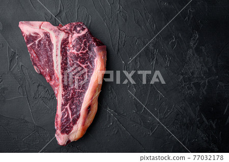 Dry aged t bone marbled beef steak, on black stone background, top view flat lay, with copy space for text 77032178