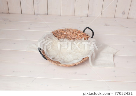 Wicker basket with white fur on a wooden background. Wicker basket with white fur on a wooden background. 77032421