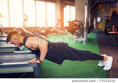 Young athletic man doing push-ups in gym. Muscular and strong gu Young athletic man doing push-ups in gym. Muscular and strong gu 77032626