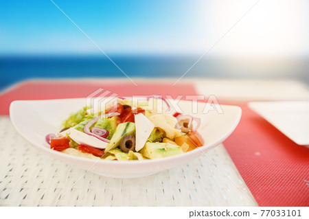 Vegetarian salad in ceramic plate on white raffia table. Vegetarian salad in ceramic plate on white raffia table. 77033101