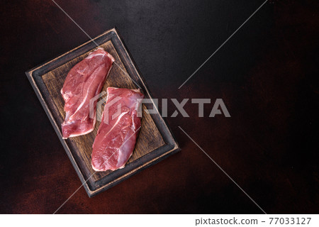 Raw duck breast with herbs and spices on a dark concrete background Raw duck breast with herbs and spices on a dark concrete background 77033127
