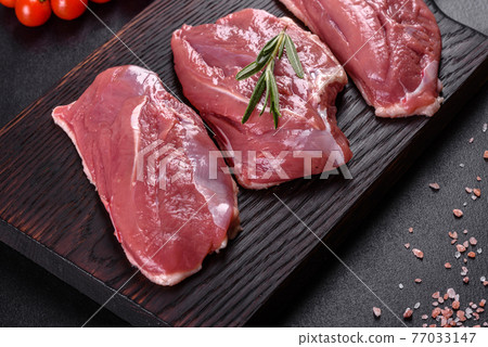 Raw duck breast with herbs and spices on a dark concrete background 77033147