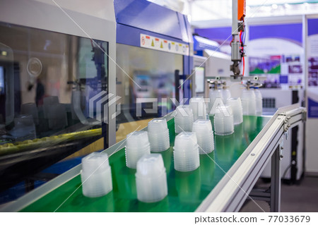 Stack of food containers on conveyor belt of plastic injection molding machine 77033679