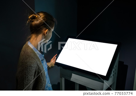 Woman using interactive empty white touchscreen display kiosk at exhibition Woman using interactive empty white touchscreen display kiosk at exhibition 77033774