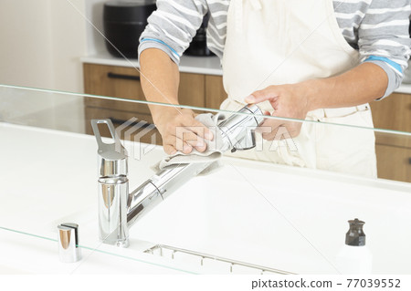 A man cleaning a kitchen faucet 77039552