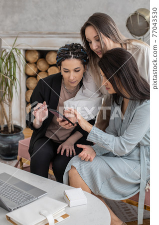 Group happy female friends chatting surfing internet use smartphone smiling having positive emotion Group happy female friends chatting surfing internet use smartphone smiling having positive emotion 77043530