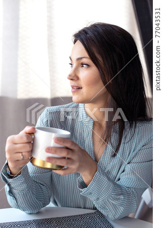 Attractive happy asian girl sitting and laughing. Drinking tea at the table. Attractive happy asian girl sitting and laughing. Drinking tea at the table. 77043531