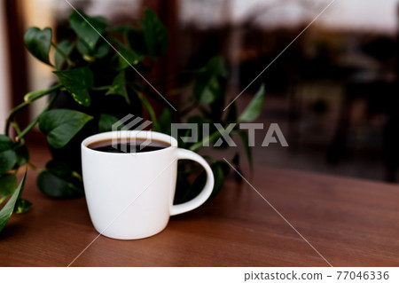 Cup of coffee or tea on the table on the wooden brown terrace during sunset Cup of coffee or tea on the table on the wooden brown terrace during sunset 77046336