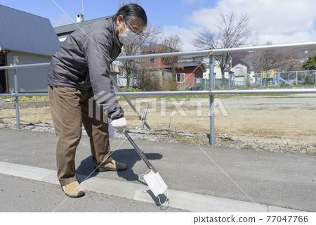 Senior man picking up a littering mask 77047766