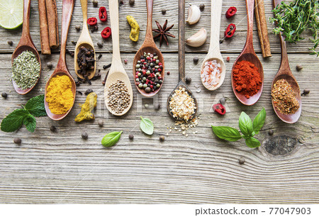 A selection of various colorful spices on a wooden table in  spoons 77047903