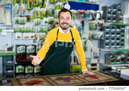 Seller displaying various items in garden equipment shop Seller displaying various items in garden equipment shop 77048047