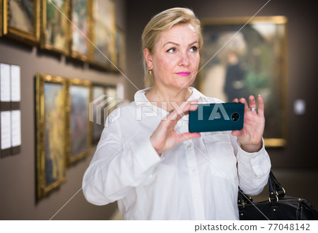 Female visitor taking picture in art gallery 77048142