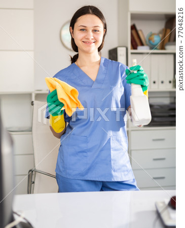 Portrait of a young woman with a rag and cleaning agent, cleaning the office 77048216