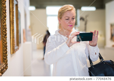 Female visitor taking picture in art gallery 77048476