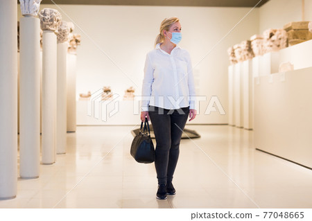 Adult woman in protective mask looking at exposition of artworks Adult woman in protective mask looking at exposition of artworks 77048665