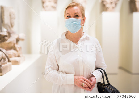 Adult woman in protective mask looking at exposition of artworks Adult woman in protective mask looking at exposition of artworks 77048666