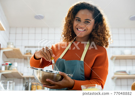 Young African American woman enjoying herself cooking in kitchen while staying at home 77048882