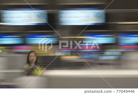 The image is blurred of people and the time signs in the airport. The image is blurred of people and the time signs in the airport. 77049446