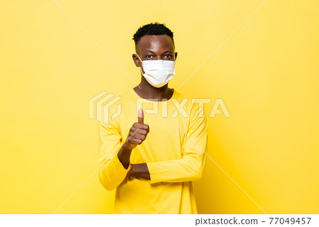 Young African man giving thumbs up and wearing face mask protecting from Corovavirus  77049457