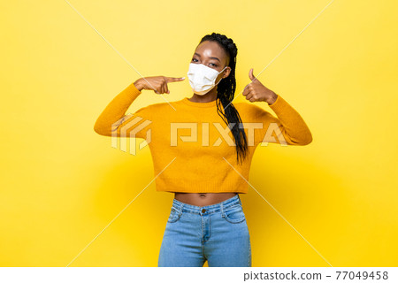 Young hygienic healthy African woman wearing face mask and giving thumbs up 77049458