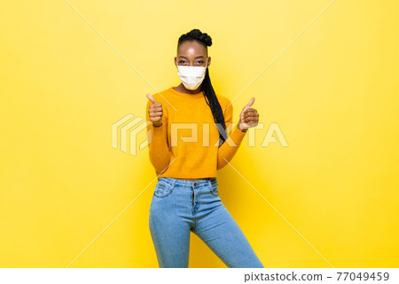 Young hygienic healthy African woman wearing face mask and giving thumbs up Young hygienic healthy African woman wearing face mask and giving thumbs up 77049459