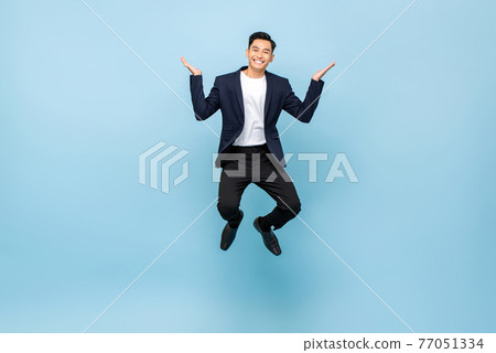 Happy Asian man jumping and smiling with open hands on isolated light blue studio background Happy Asian man jumping and smiling with open hands on isolated light blue studio background 77051334