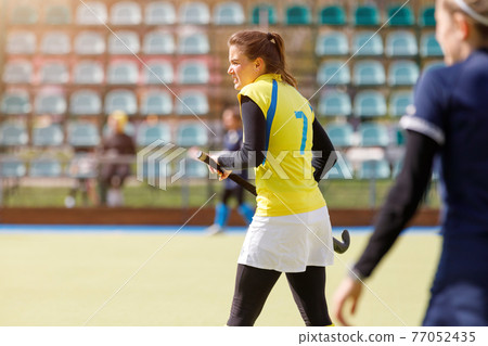 Young field hockey girl player with stick at pitch Young field hockey girl player with stick at pitch 77052435