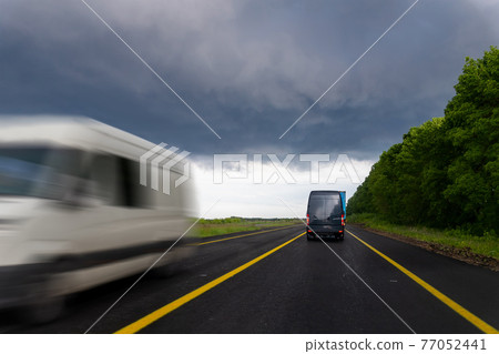 Bacl of delivery small shipment cargo courier van moving fast on wet highway road to city urban suburb against rainy cloudy sky . Business distribution and logistics express service. Mini bus motion Bacl of delivery small shipment cargo courier van moving fast on wet highway road to city urban suburb against rainy cloudy sky . Business distribution and logistics express service. Mini bus motion 77052441