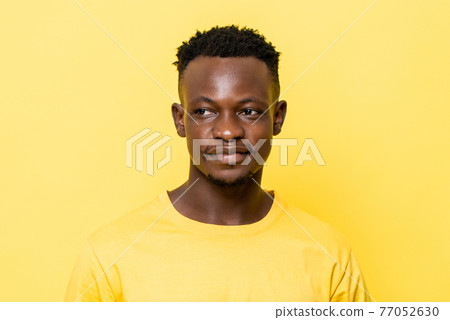 Close up portrait of young smiling African man looking away on isolated yellow studio background 77052630