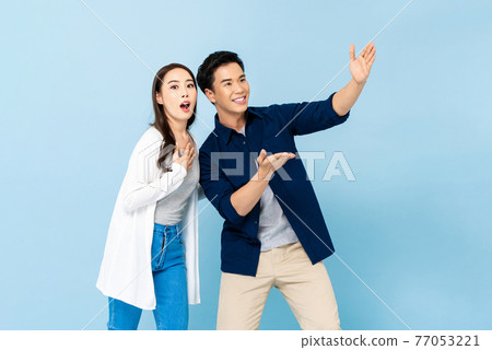 Shocked amazed Asian couple pointing hands up to empty space above on isolated light blue background 77053221
