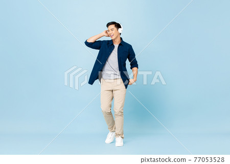 Smiling young handsome Asian man listening to music with wireless headphones Smiling young handsome Asian man listening to music with wireless headphones 77053528