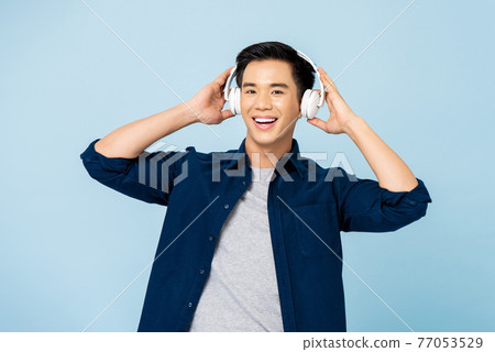 Happy smiling young handsome Asian man listening to music with wireless headphones Happy smiling young handsome Asian man listening to music with wireless headphones 77053529