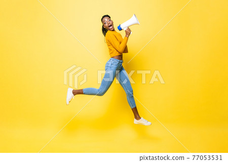 Jumping portrait of shocked young African American woman holding megaphone making announcement 77053531