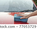 Man cleaning red automobile with blue sponge at car wash with copy space for text 77053729