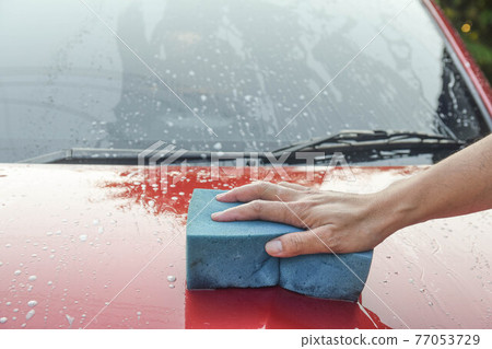 Man cleaning red automobile with blue sponge at car wash with copy space for text 77053729